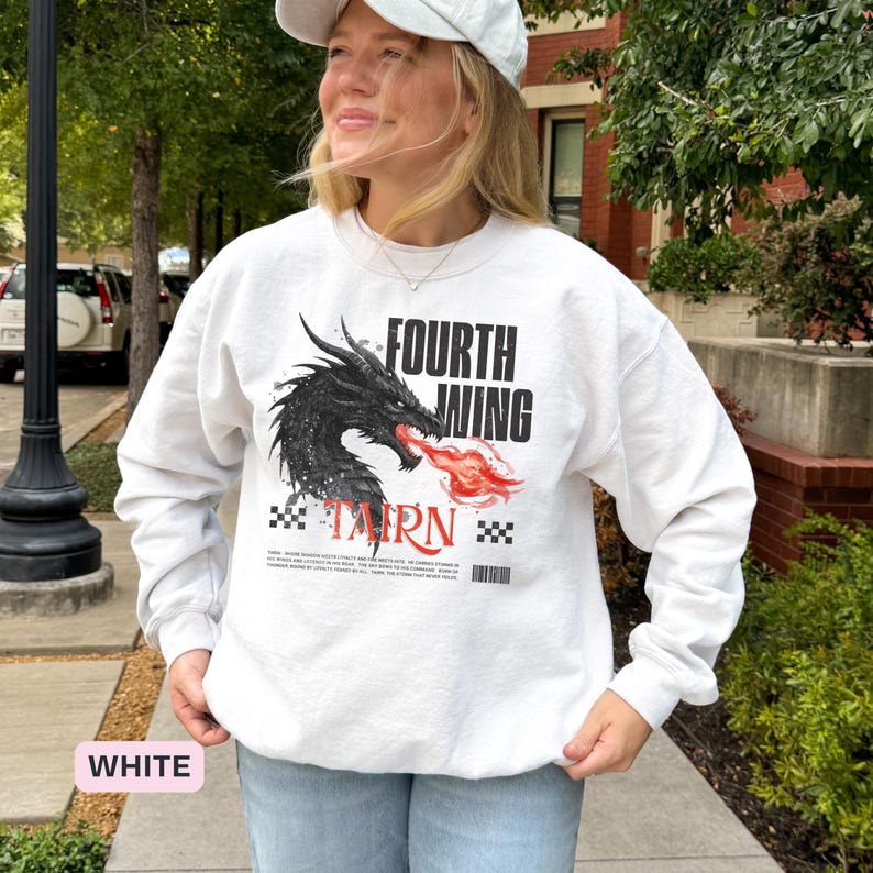 K&ouml;nnte beinhalten: Wei&szlig;es Sweatshirt mit einem schwarzen Drachenmotiv, der rote Flammen speit, mit dem Text "FOURTH WING" und "TAIRN". Das Design beinhaltet ein Schachbrettmuster und Text am unteren Rand. Es ist ein lang&auml;rmeliges Rundhals-Sweatshirt.