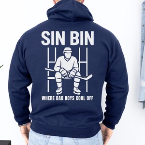 May include: Navy blue hoodie with a white graphic on the back. The graphic features the words "SIN BIN" above an illustration of a hockey player sitting on a bench, with the text "WHERE BAD BOYS COOL OFF" below.