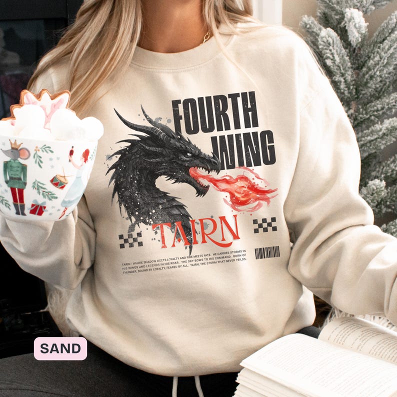 K&ouml;nnte beinhalten: Sandfarbenes Sweatshirt mit einem schwarzen Drachen, der rotes Feuer speit, mit dem Text "FOURTH WING" und "TARN". Das Design enth&auml;lt einen Barcode und Text. Ein l&auml;ssiges Kleidungsst&uuml;ck.