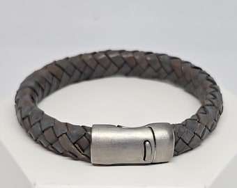 May include: A braided leather bracelet with a silver clasp. The bracelet is a dark grey colour.