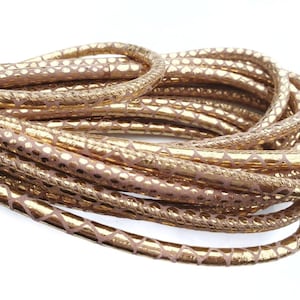 Może przedstawiać: Zbliżenie na szpulę ze złotym sznurkiem skórzanym z wzorem skóry węża. Sznurek jest zwinięty i gotowy do użycia w projektach rękodzielniczych.