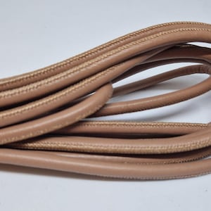 May include: A close-up of a coil of light brown leather cord with a subtle stitching detail.