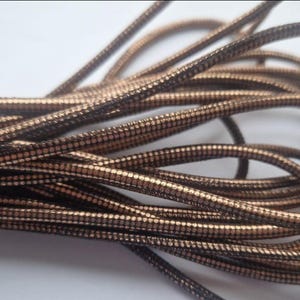 Może przedstawiać: Zbliżenie na szpulkę brązowego i złotego sznurka. Sznurek ma fakturowany, tkany wygląd i idealnie nadaje się do prac rękodzielniczych.