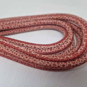 Op de afbeelding: Een close-up van een rood en wit gepatroneerd leren koord. Het koord is gemaakt van zacht, soepel leer en heeft een subtiele glans.