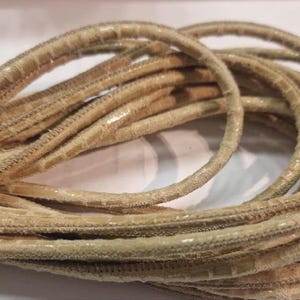 Może przedstawiać: Zbliżenie beżowego sznurka skórzanego o fakturowanej powierzchni. Sznurek jest zwinięty i wydaje się być wykonany z cienkich pasków skóry.