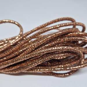 May include: A spool of metallic gold cord with a textured surface. The cord is coiled and ready for crafting projects.