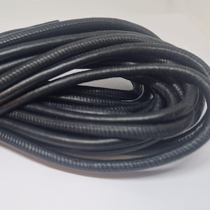 May include: A close-up of a coil of black leather cord. The cord is smooth and flexible, and it is perfect for crafting projects.