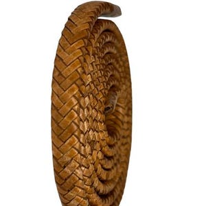Op de afbeelding: Een opgerolde, bruine leren riem met een geweven patroon. De riem is spiraalvormig, wat de ingewikkelde textuur en het vakmanschap laat zien. De gesp is aan de bovenkant zichtbaar en het algehele ontwerp suggereert een focus op duurzaamheid en stijl.