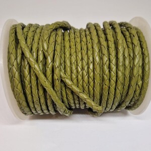 May include: A spool of olive green braided leather cord. The cord is approximately 5mm wide and is perfect for crafting projects.
