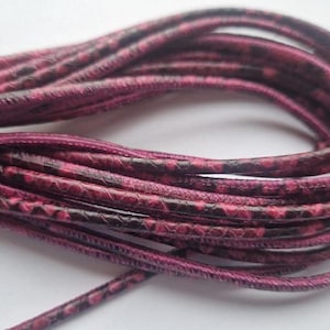 Könnte beinhalten: Nahaufnahme eines rosa-schwarzen Lederkordels. Das Kordel ist aus einem dünnen, flexiblen Material gefertigt und hat ein Schlangenhautmuster.