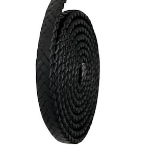 Puede incluir: Un cordón de cuero trenzado negro enrollado sobre un fondo blanco. El cordón está tejido apretadamente, con un extremo redondeado que se extiende hacia arriba. La textura del cuero es visible, y la apariencia general es elegante y moderna.