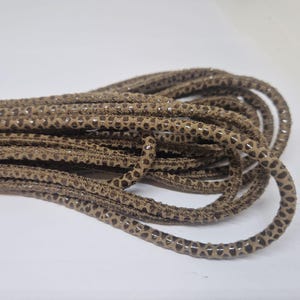 Może przedstawiać: Zbliżenie na brązowy sznurek skórzany z fakturowanym wzorem. Sznurek jest zwinięty i gotowy do użycia w projektach rękodzielniczych.