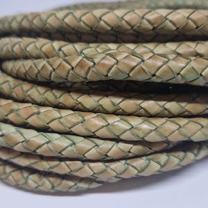 Può includere: Primo piano di un cordoncino in pelle intrecciato di colore verde chiaro e beige. Il cordoncino è intrecciato a forma di rombo.