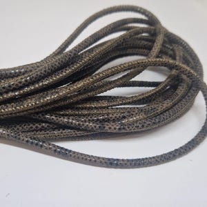 Może przedstawiać: Zbliżenie na kłębek brązowego i czarnego sznurka skórzanego. Sznurek ma fakturowaną powierzchnię i jest idealny do prac rękodzielniczych.