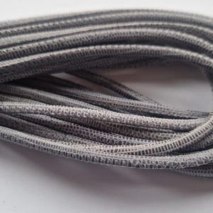 Może przedstawiać: Szary sznurek elastyczny z fakturowaną powierzchnią. Sznurek jest zwinięty i gotowy do użycia w pracach ręcznych lub innych projektach.