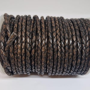 May include: A spool of dark brown braided leather cord. The cord is tightly wound around a white plastic spool. The leather has a textured appearance with variations in color, suggesting a natural finish. The cord is suitable for jewelry making or crafting.