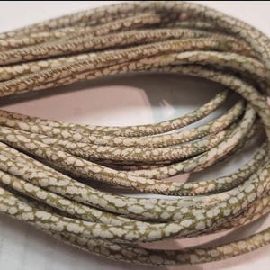 Może przedstawiać: Zbliżenie na szpulkę beżowego sznurka z białym wzorem. Sznurek jest wykonany z miękkiego, elastycznego materiału i ma fakturowaną powierzchnię.