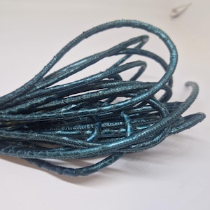 Może przedstawiać: Sznur ze skóry w kolorze turkusowym, skręcony i zwinięty w rulon. Sznur ma fakturowaną powierzchnię, co nadaje mu niepowtarzalny wygląd.