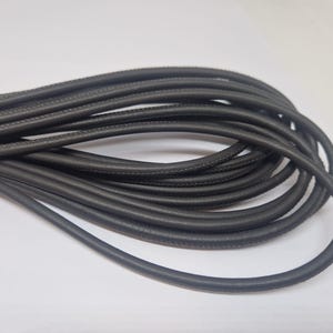Può includere: Un primo piano di un rotolo di cordoncino in pelle nera. Il cordoncino è liscio e flessibile, ed è perfetto per progetti di artigianato.