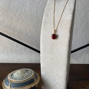 May include: A gold chain necklace with a red gemstone pendant on a white velvet display stand.