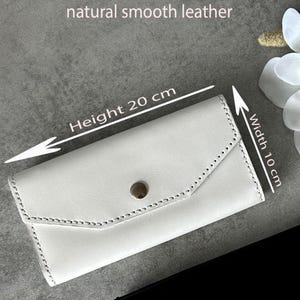 May include: A white leather wallet with a button closure. The wallet is 7.9 inches in height and 3.9 inches in width. The text "natural smooth leather" is visible at the top. The wallet has a stitched design.