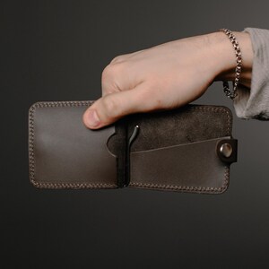 May include: A brown leather wallet with a money clip and a small pocket. The wallet is open and the inside is visible.