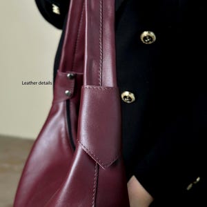 May include: Close-up of a burgundy leather handbag with a shoulder strap. The bag features detailed stitching and a sleek design. The text "Leather details" is visible.