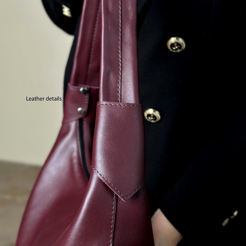 May include: Close-up of a burgundy leather handbag with a shoulder strap. The bag features detailed stitching and a sleek design. The text "Leather details" is visible.