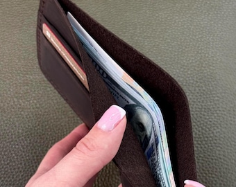 May include: A brown leather wallet with a flap that opens to reveal a cash pocket and card slots. The wallet is being held open by a hand.