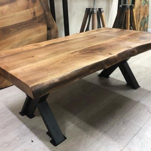 May include: A wooden coffee table with a live edge top and black metal X-shaped legs.