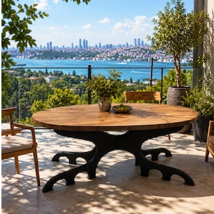 May include: An oval wooden dining table with a natural grain finish and a black metal base featuring four curved, branching legs. The table is positioned outdoors on a stone patio, accompanied by wooden chairs with light-coloured cushions.