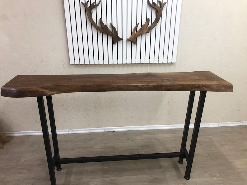 May include: A console table featuring a natural live edge dark brown wooden top with a smooth finish. The table is supported by a black metal frame consisting of four vertical legs connected by a horizontal bar near the base for added stability.