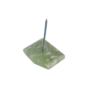 May include: A light green, rectangular incense holder made of stone. A single blue incense stick is inserted into a hole in the center. The stone has a natural, textured appearance.
