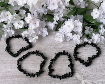 May include: Four black gemstone chip bracelets on a white wooden surface. The bracelets are made of small, irregular shaped black stones.