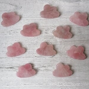 Könnte beinhalten: Zehn rosa Rosenquarz-Wolken-Steine auf einer weißen Holzoberfläche.