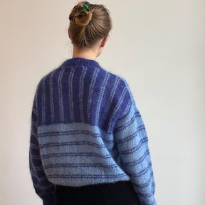 May include: A blue and light blue striped sweater. The sweater has a crew neck and long sleeves. The top portion of the sweater is a darker blue, while the bottom portion is a lighter blue. The sweater is made of a soft, fuzzy material.