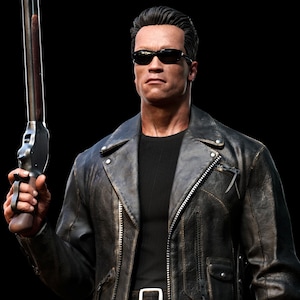 May include: A man wearing a black leather jacket and sunglasses holds a shotgun in his right hand. The background is black.
