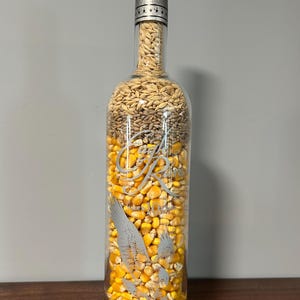 May include: A clear glass bottle filled with corn kernels, barley, and rye grains. The bottle has a silver label with the text "Eagle Rare" and a graphic of a flying eagle.