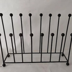 May include: A black metal boot rack with a rectangular base and vertical rods topped with round spheres. The rack has a series of vertical rods, some with a sphere in the middle, and is designed to hold multiple pairs of boots.