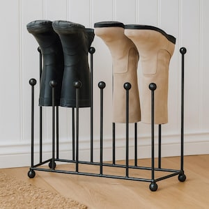 May include: A black metal boot rack holding four pairs of boots. Two pairs are black rubber boots, and the other two are tan suede boots. The rack has a rectangular base with vertical supports topped with decorative spheres.