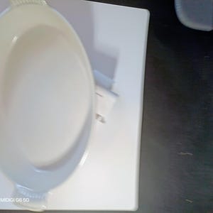 May include: White oval ceramic baking dish with handles, on a white rectangular surface. The dish has a smooth, glossy finish. The image is taken from an overhead perspective.