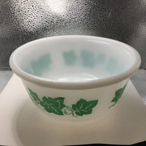 May include: White glass bowl with a green leaf pattern around the exterior. The bowl has a rounded shape and a smooth, glossy finish. The leaf design is a repeating pattern of stylized green leaves.