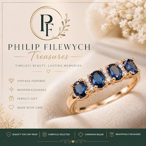 May include: A gold ring featuring five oval, dark blue gemstones interspersed with smaller, clear stones. The ring is set against a soft, neutral background with the text "PHILIP FILEWYCH Treasures" and other text.