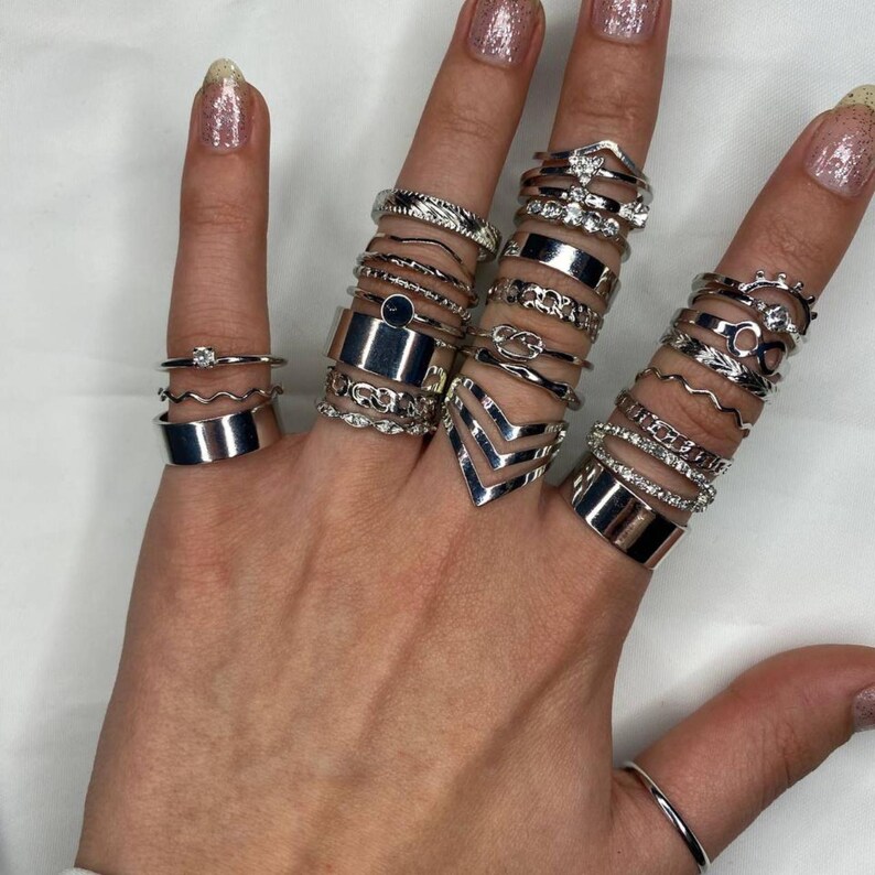 May include: A hand model wearing a stack of silver rings on multiple fingers. The rings are various styles, including geometric, chain, and open designs.