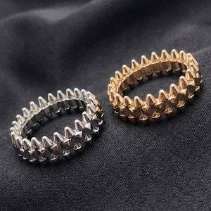 May include: Two rings with a spiked design. One ring is silver, and the other is gold. The rings are set against a dark background. The rings are likely made of metal and are designed to be worn on a finger.