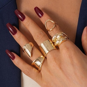 May include: A white ceramic mug with a black handle and the text "But First, Coffee" in a bold, black font. The mug is set against a blurred background, suggesting a cosy setting.