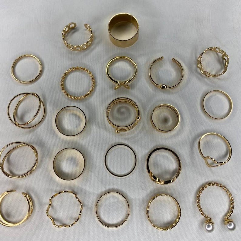 May include: A set of 21 gold-toned rings, featuring a variety of styles, including simple bands, twisted designs, and open rings with pearl accents.