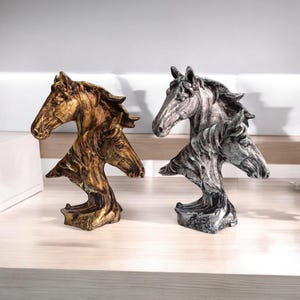 Könnte beinhalten: Zwei dekorative Pferdekopfskulpturen, eine in Gold und eine in Silber, mit einem mehrschichtigen Design aus mehreren Pferdeköpfen.