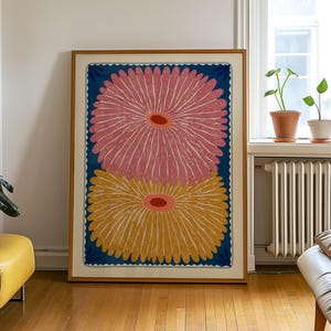 May include: A rectangular framed wall art piece featuring two large, stylized flower illustrations stacked vertically. The top flower is pink and the bottom flower is yellow, both set against a deep blue background with a scalloped border.