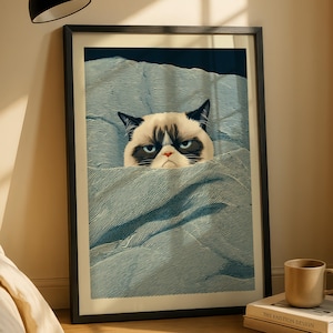 Peut inclure: Impression encadrée d'un chat grincheux au visage noir et blanc, émergeant d'une couverture bleue. Le chat a un air renfrogné et des yeux bleus perçants. L'œuvre est présentée dans un cadre noir, créant une pièce humoristique et expressive.